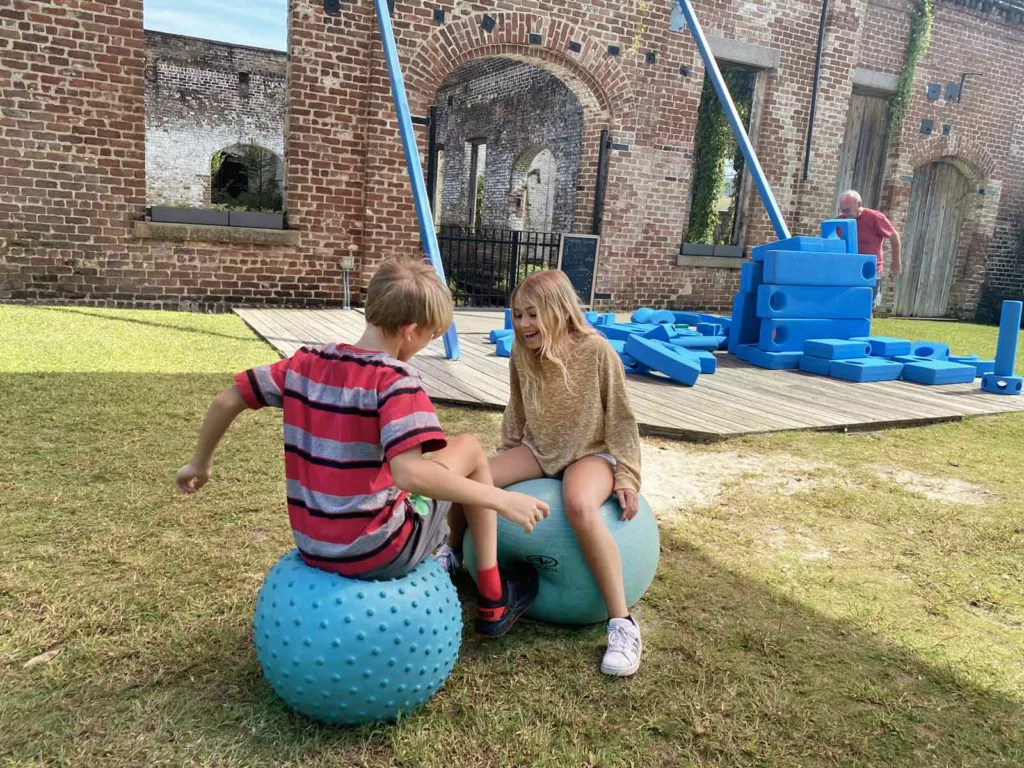 two kids bouncing on a yoga ball at the Savannah children's outdoor museum in a grassy area