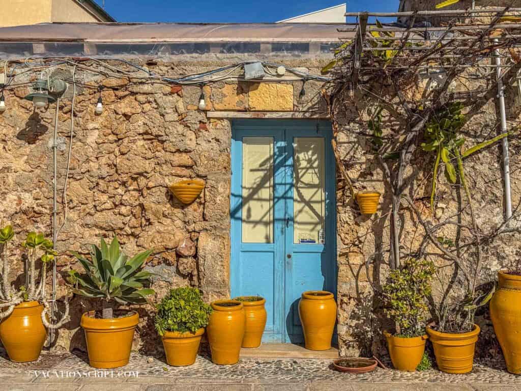 turquoise front door with orange potted plants lining the ground of this Sicilian front door