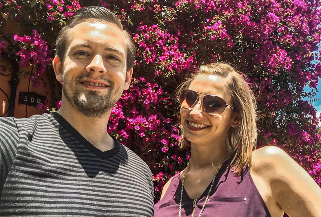 A couple enjoying their exploration of Lombard Street in San Francisco, pausing to strike a pose in front of the enchanting floral trees that line this renowned winding road.