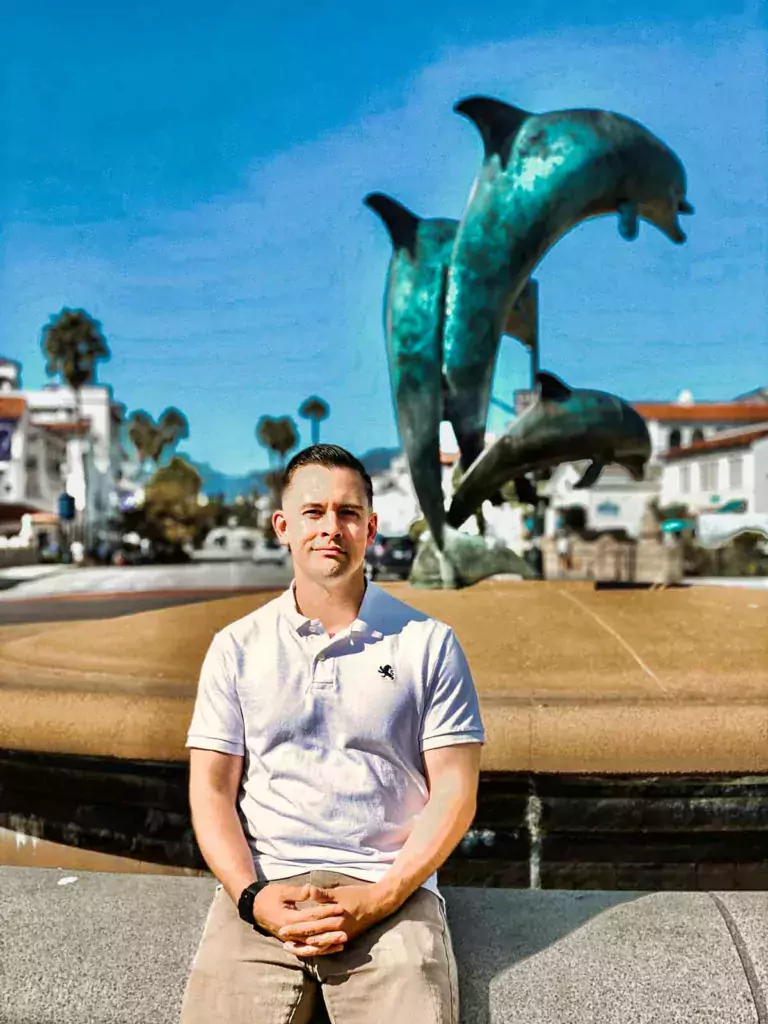 A man posing confidently in front of the Dolphin Fountain in Santa Barbara, California.