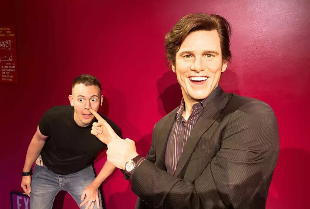 Jim Carrey's wax figure humorously pointing towards a man who is positioned in a way that gives the illusion of Jim Carrey picking the man's nose at Madame Tussauds wax museum in Hollywood.