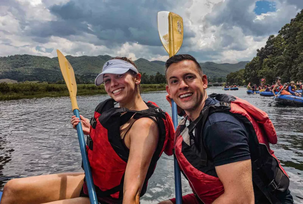 A couple having fun with their paddles during river rafting in the beautiful Watauga River with the hills of Tennnessee in the background.