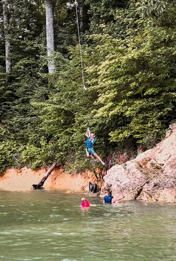 Young boy swinging from the cliff's edge into Watauga Lake with his family.