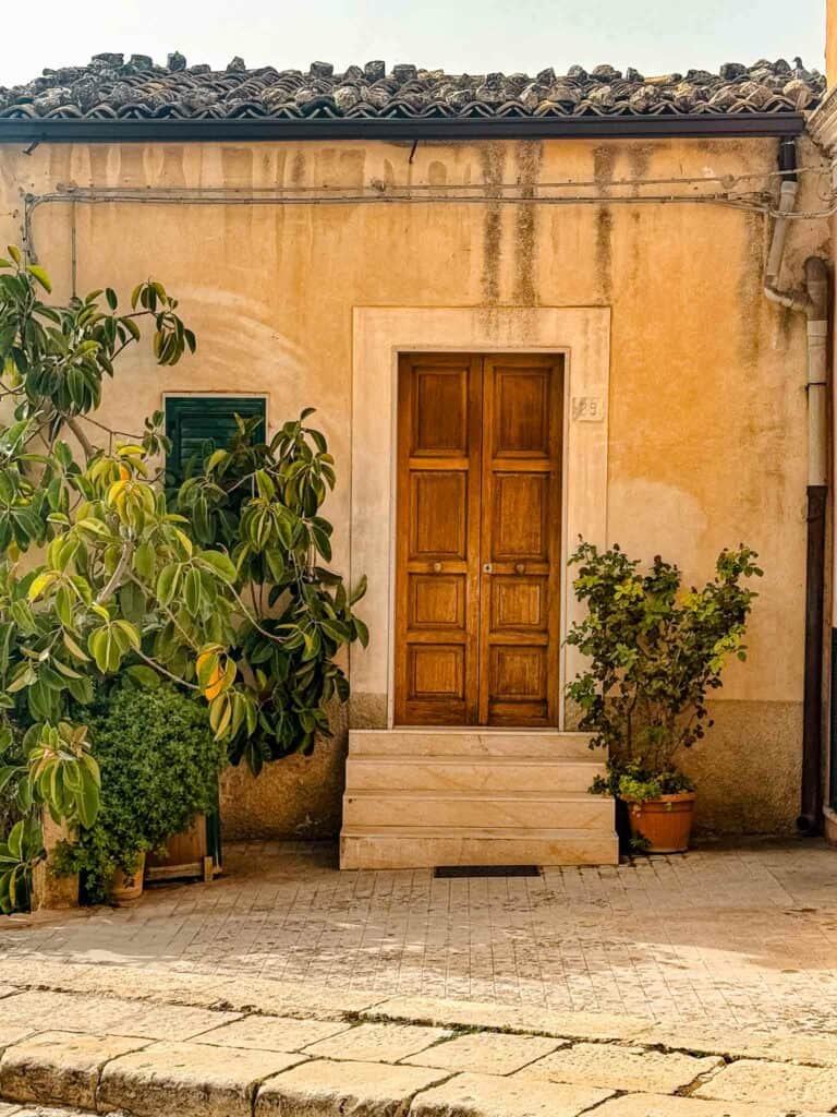 ragusa sicily front wooden door with plants surrounding the steps up to the door