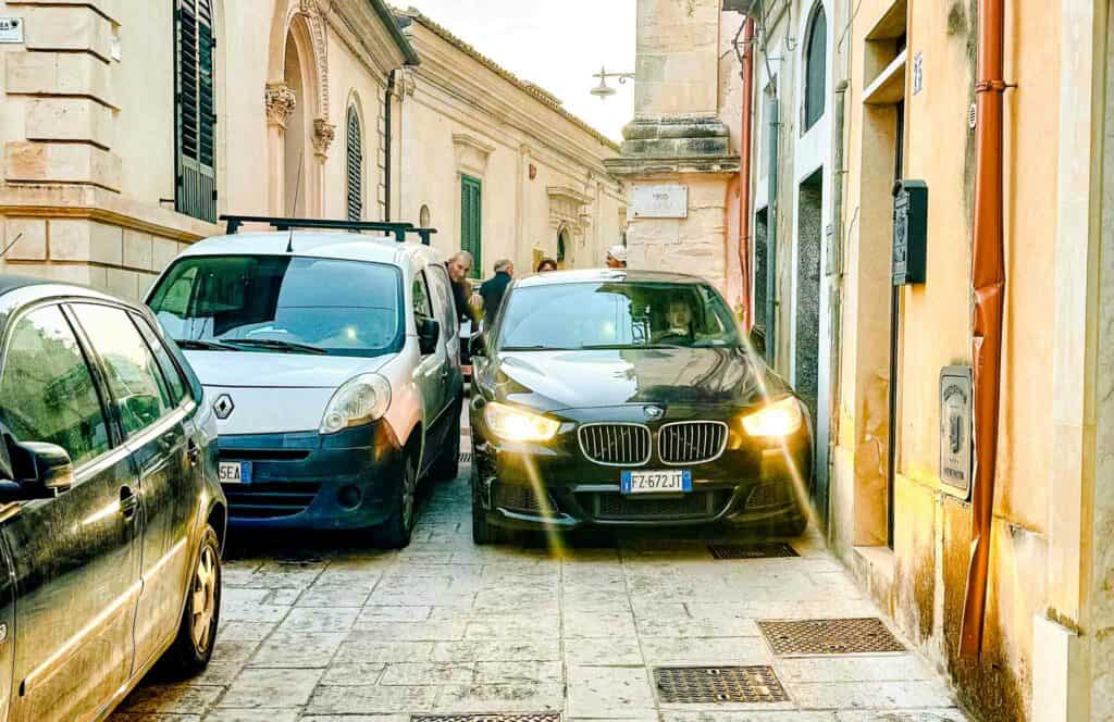 squeezing a large car past historical Italian buildings and another car