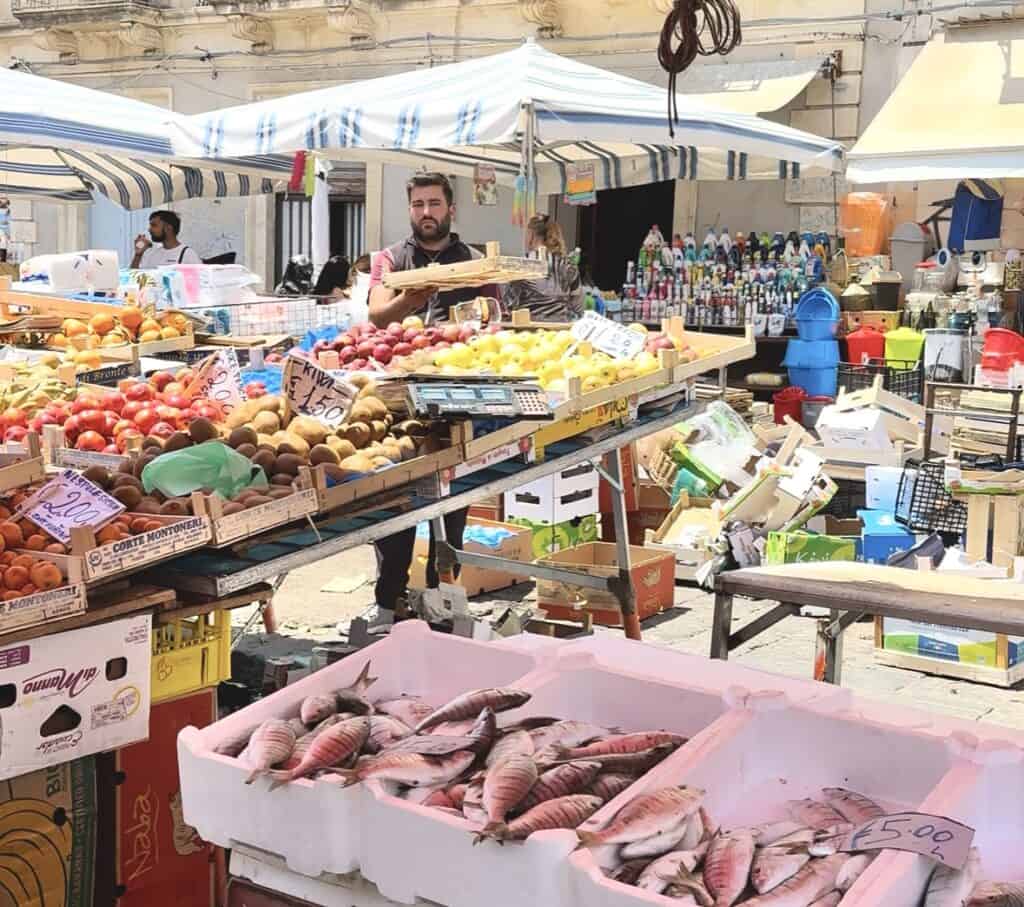 Bustling flea market at Charles Albert of Savoy Square in Catania, lively with shoppers haggling over deals and browsing knockoff brands.