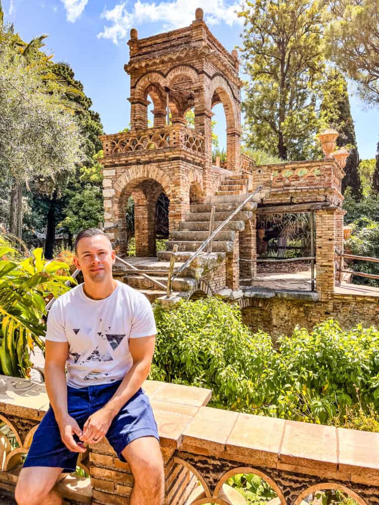 Smiling man sitting on a balcony overlooking Trevelyan Park, a public garden in Taormina, Sicily.