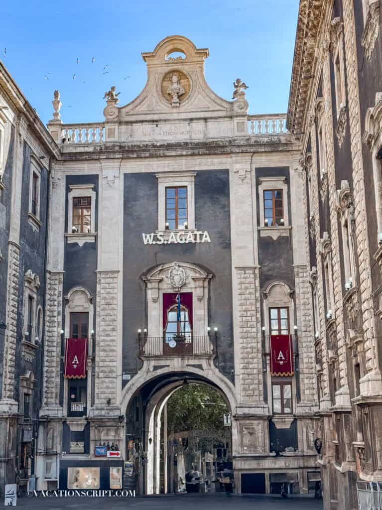 Porta Uzeda decorated with red banners featuring the letter ‘A’ and illuminated letters spelling ‘W.S. Agata’ during the Sant’Agata festival.