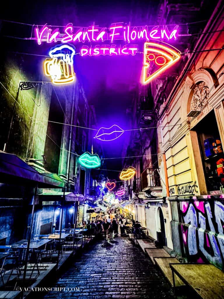 Neon string lights featuring lips, hearts, beer, martini glasses, pizza, and more in the lively Via Santa Filomena district, a popular spot for food lovers in Catania.