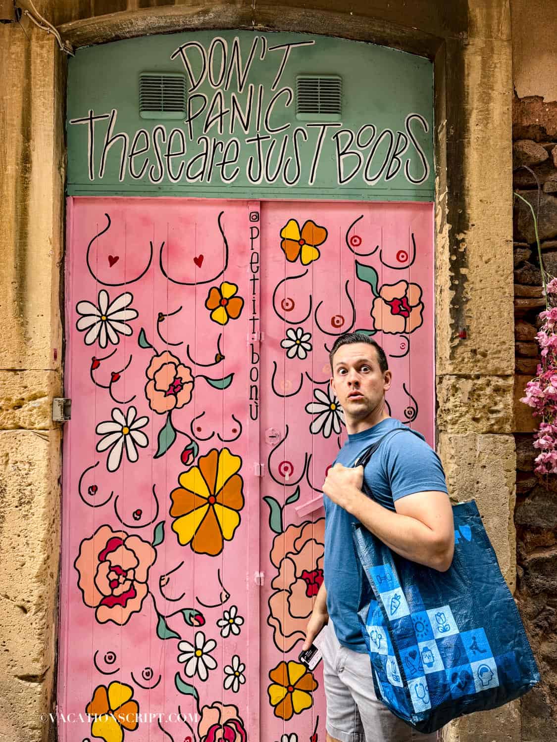 Colorful pink and green floral door at Petit Bonu painted with humorous breasts mural in a back alley of Catania, featuring the phrase ‘Don’t panic, these are just boobs.’